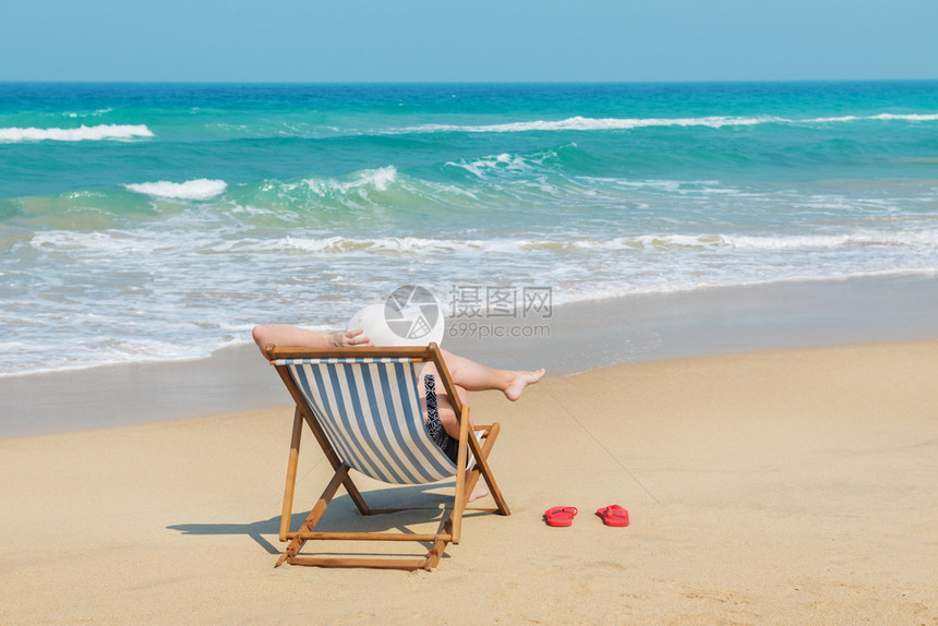 自然海洋坐在甲板椅子上度假和旅行概念的沙滩上穿着白色日光浴的快乐女人孩图片