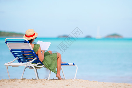 书的海洋椅子气候享受年轻女在海滩上阅读关于沙的chaiiselounge的书背景