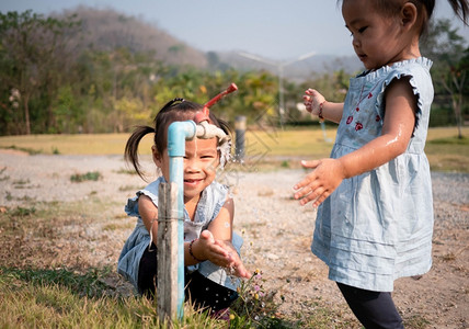 亚洲小女孩和妹用花园的钢水龙头洗手从花园里肖像液体公园图片