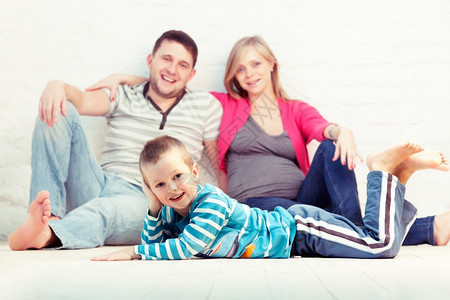 小男孩和他父母在墙旁边的地板上母亲怀孕了儿子微笑地面图片