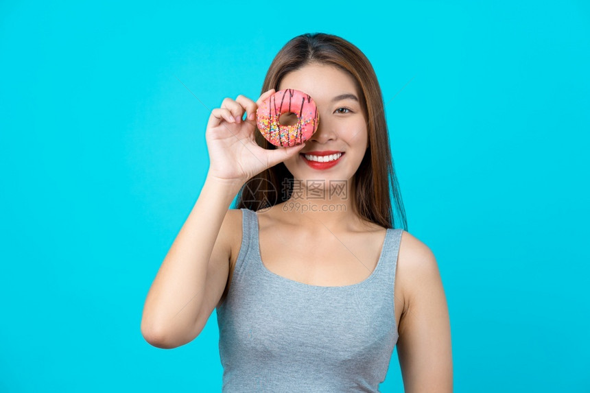 节食吃有吸引力的亚洲年轻女在孤立的蓝色背景体重减避免垃圾食品用于饮和健康概念复制空间和工作室时微笑并玩着甜圈畅快图片