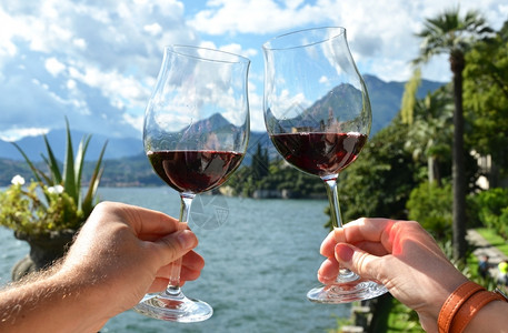 山阿尔卑斯景观意大利科莫湖两杯葡萄酒手握着两个葡萄玻璃杯图片