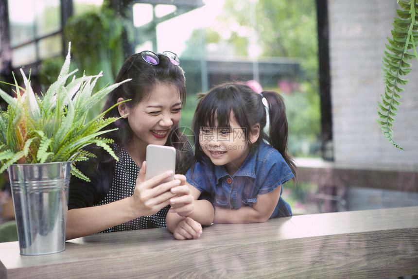 人们青年药片正在家中客厅寻找智能电话屏幕的年青亚洲小妇幼女和儿童图片