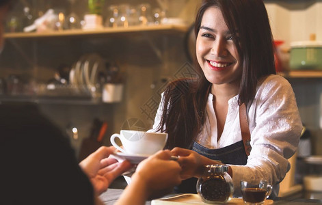 茶食物白种人美丽的亚洲女律师协会向在反酒吧背景的顾客提供热咖啡微笑着的妇女和工作以及图片