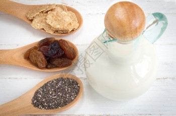 一组葡萄干全小麦片和木勺中的奇阿种子和白木背景的牛奶勺子白色谷物图片