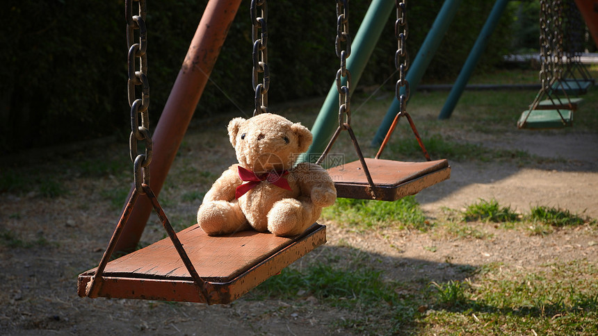 在公园操场的秋千上坐着小泰迪熊表面晨光照耀着小泰迪熊的阳光童年目自然图片