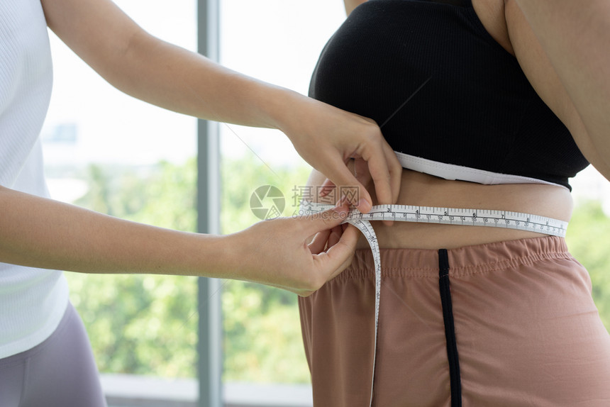 年轻女训练员测量超重妇女脂肪层腰带健壮脂肪团康计算图片