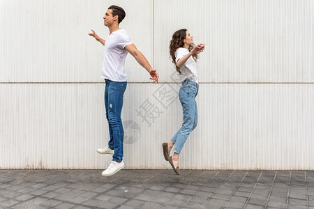 晴天年轻夫妇背靠着白色城墙回跳来去跃夏天图片