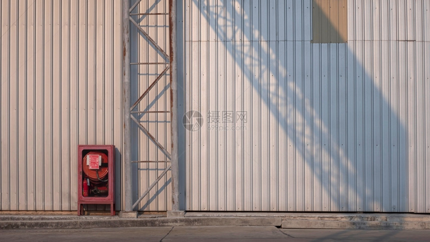 古老的红色应急柜子和在水泥地板上有阳光和影子的铁板墙壁表面水泥地板上锈制金属高地路标牌结构工厂建筑的金属板墙壁表面有阳光和阴影工图片