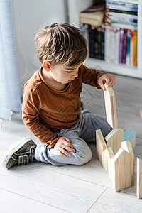 全龄化在木制或黑乙烯层化的地板上单靠开发创造力的最高视野用木玩具砖打房子形状的木玩具砖耍小天主教男孩的家庭全视仅靠木制或维尼基胶状的地背景
