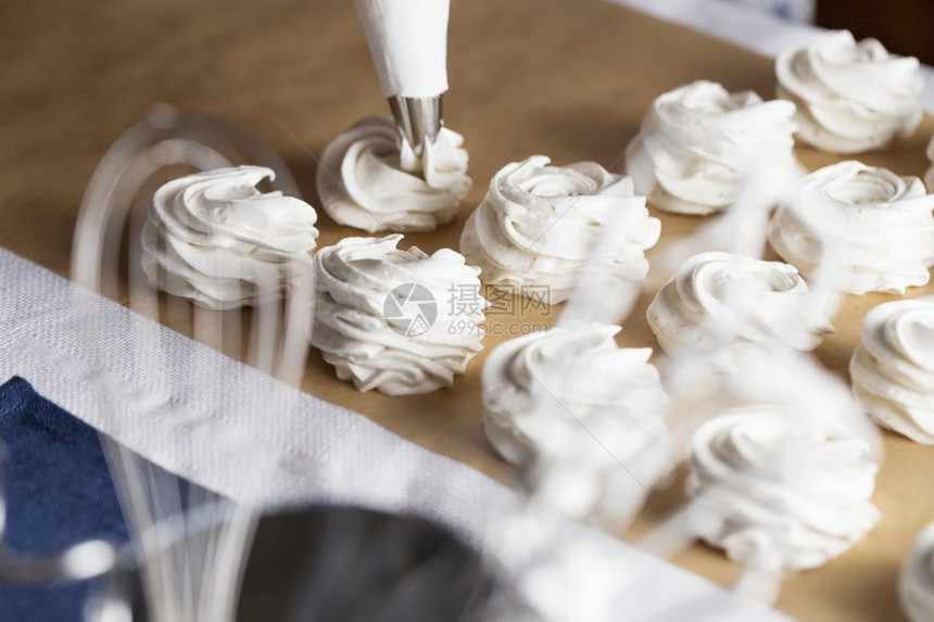 在糕点店的厨房里使棉花糖贴紧厨师手的过程用甜食袋奶油和纸年轻的店铺生产图片