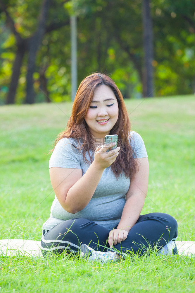 在公园户外使用手机的快乐肥胖亚洲女人士草地们图片