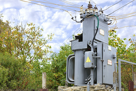 行业电缆一个古老的变压器电站在秋天花园的中间一个用金属网格围住的秋天花园与蓝云空变换器电站对面压器电站在花园中央一个蓝色云层对面图片