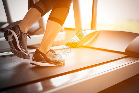 动主题素材成人们女健康与锻炼活动概念健身和强力训练主题在健身房运行机或动场上跑步的健身女孩腿下部体用阳光照射温暖的语调背景