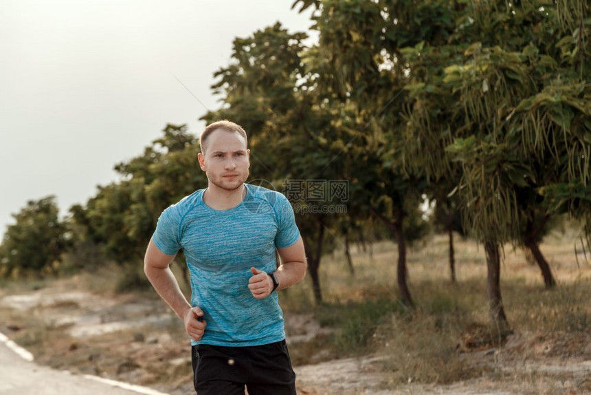 移动慢跑穿着蓝色T恤和黑短裤的白人男子肖像他们在日落时沥青轨道上培训和运行身体的图片