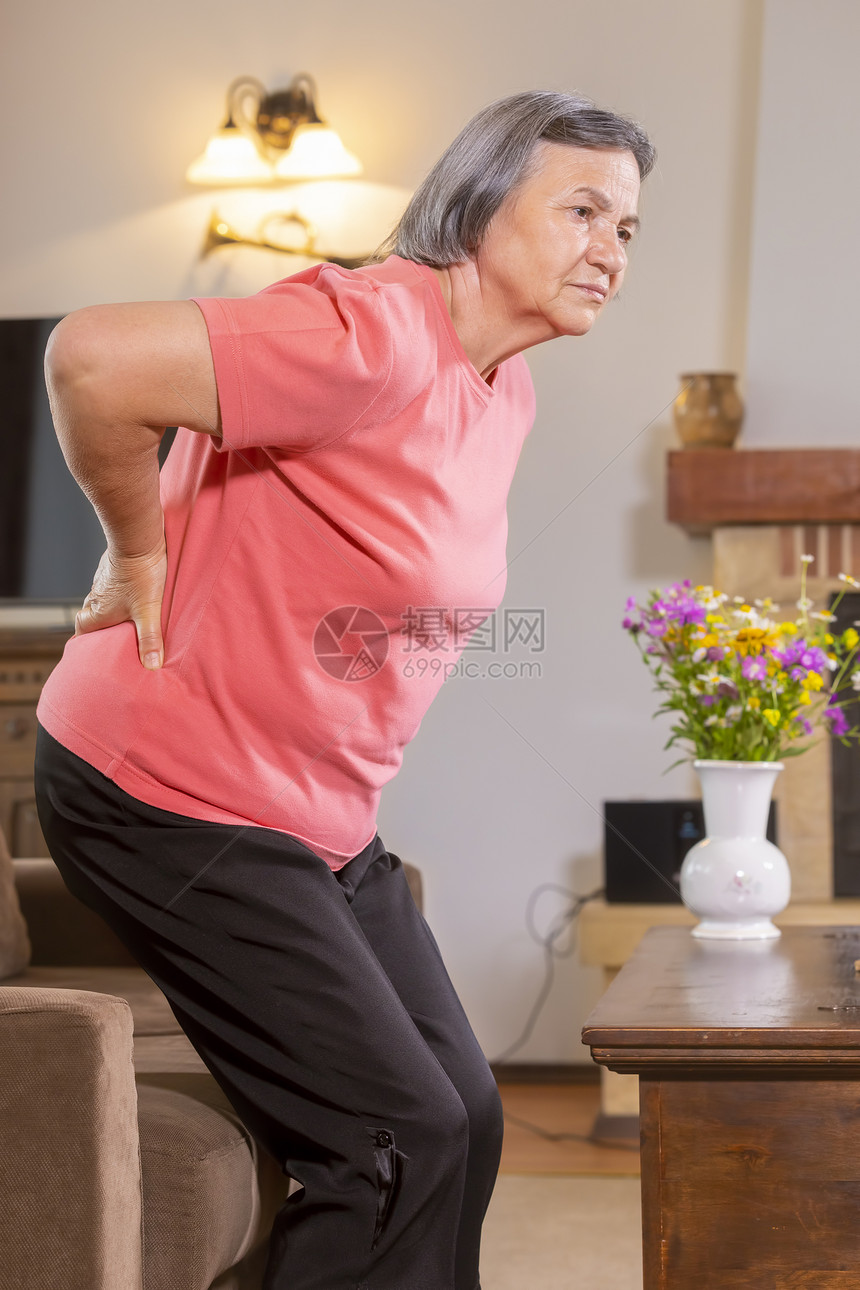 健康疾病家中患有背痛的女年长妇用手往下反按摩感到疲惫站在起居室里骨软病图片