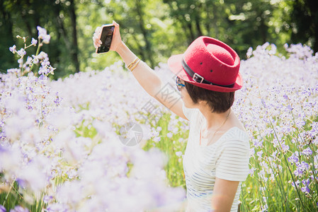 紫色蝴蝶结帽子欢乐的年轻女子用她智能手机在紫罗兰草地上自拍肖像工作室时髦背景