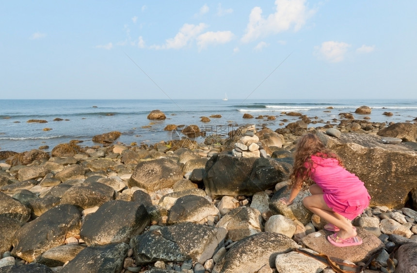 闲暇人类快乐的美丽小女孩爬在岩石海岸边的上图片