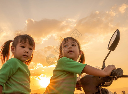 肖像姐在日落的天空背景下和妹坐在摩托车上可爱的小女孩儿户外图片