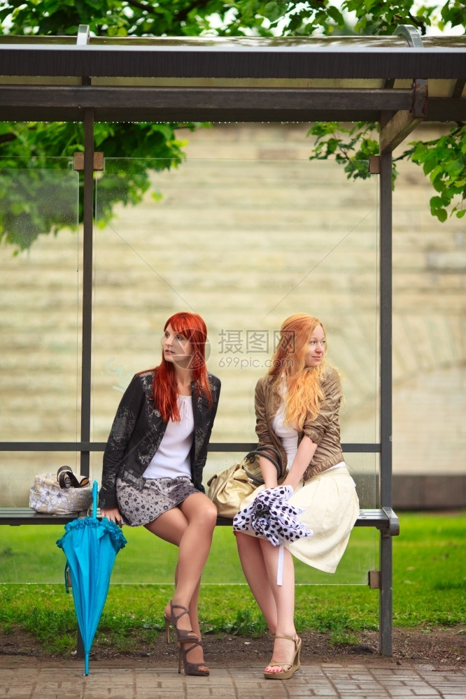 2个女孩在雨季的公共汽车站女孩们夏天高跟鞋图片