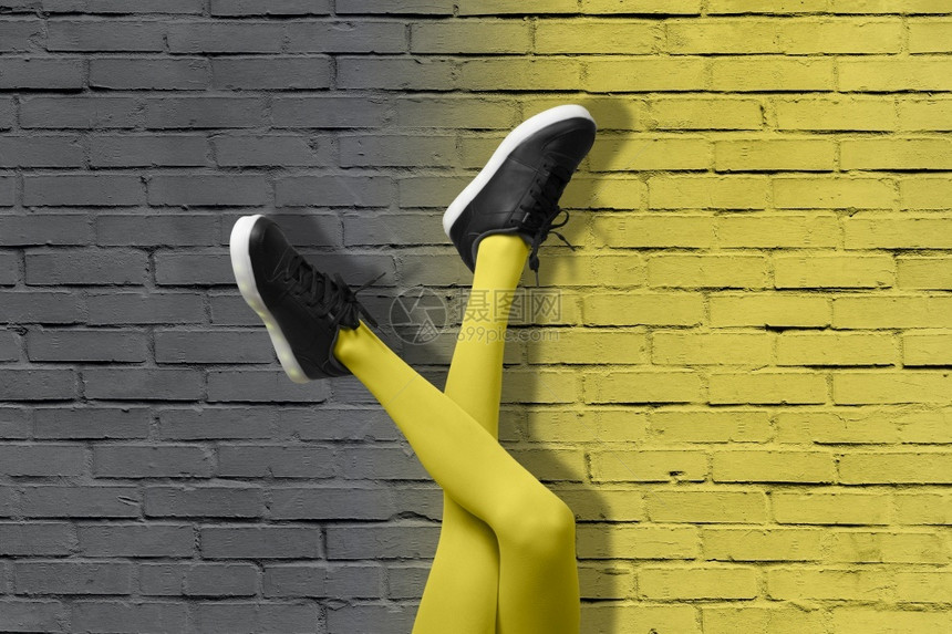 女流行音乐201年流行艺术概念的颜色201新的黑色女运动鞋在细长的女孩腿上穿着黄色紧身裤在渐变的黄色和灰砖墙的背景上201年概念图片