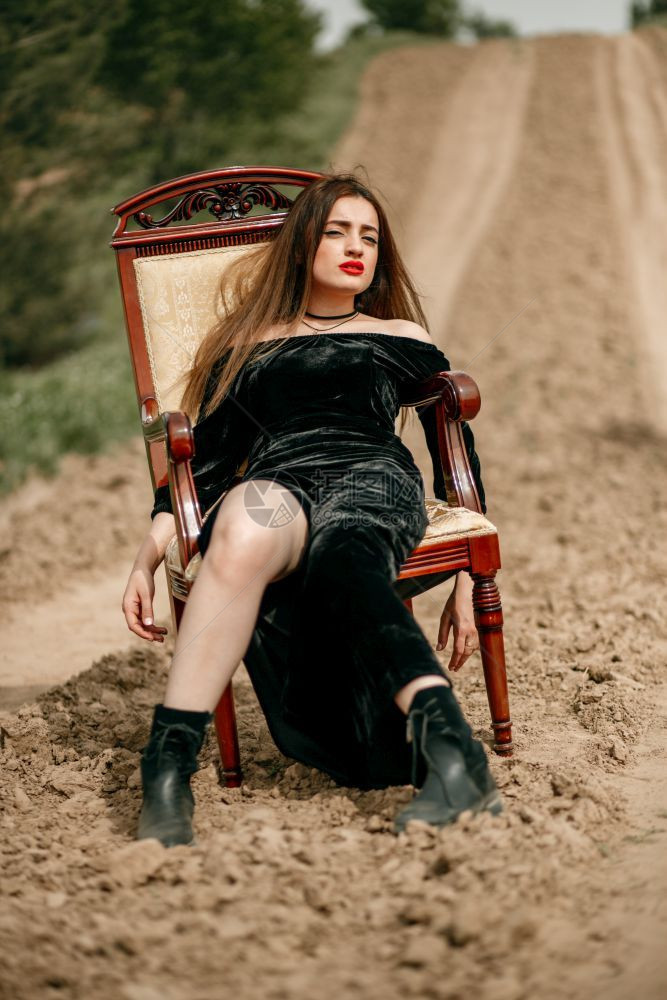 为了身着黑裙子的漂亮年轻美女为一位坐在沙路上经典扶手椅的摄影师做姿势健康快乐的图片