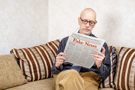 姆沙涅茨新闻纸一名戴眼镜的男人坐在家里沙发上看报纸导假新闻冒消息LoremImpsum文本出版打印背景