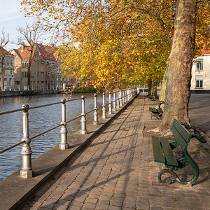 游客建成靠近布鲁日运河的班子在多彩树木下比利时城市的图片