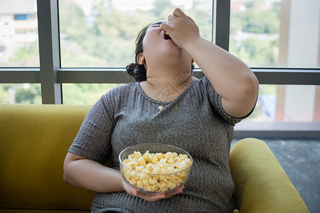 胖的好吃超重妇女和亚洲孩在家沙发上享受食物吃成人图片