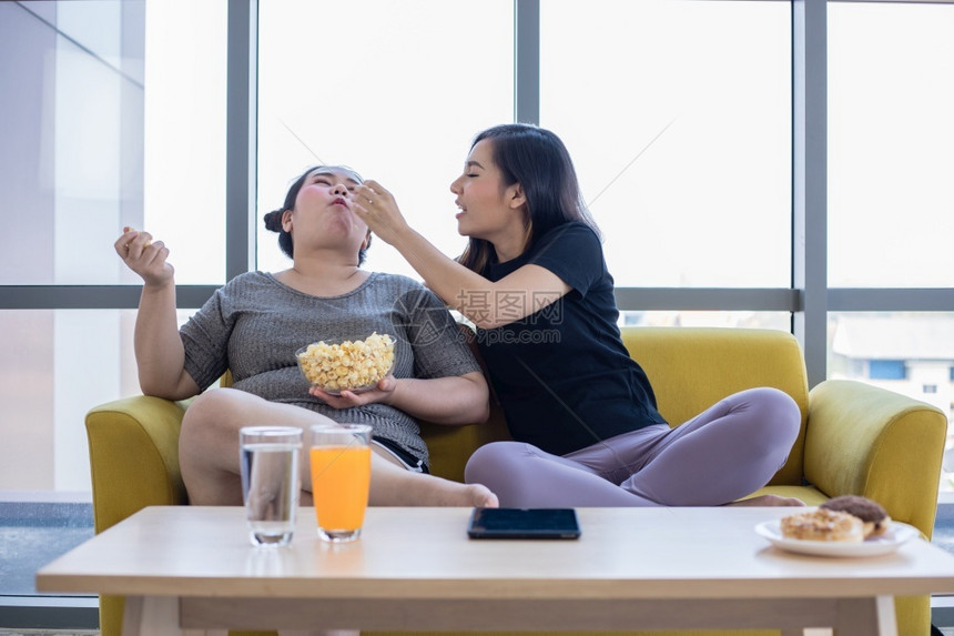 美味的一顿饭超重妇女和亚洲孩在家沙发上享受食物吃不良图片