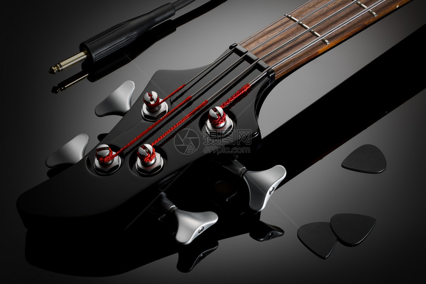 棕色的目电贝斯吉他有声电缆和接听器的头盘紧贴在黑的电贝吉尔他黑色接客和紧靠旁边的Glossy背景反射低键抛光图片