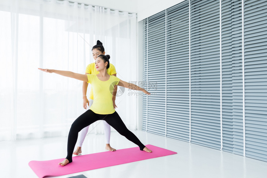 班级快乐的两名亚洲年轻妇女在健身房练习瑜伽穿黄色礼服或与训练员和实习者一起表演冥想健康生活方式和健康概念运动图片