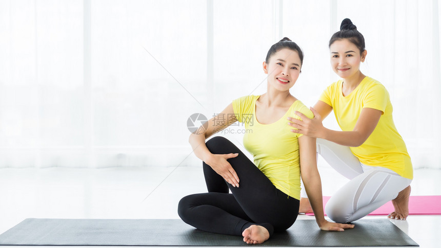 手黄色的两名亚洲年轻妇女在健身房练习瑜伽穿黄色礼服或与训练员和实习者一起表演冥想健康生活方式和健康概念裙子图片