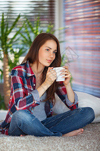 请享用马克杯微笑年轻女子在家沙发上喝咖啡茶图片