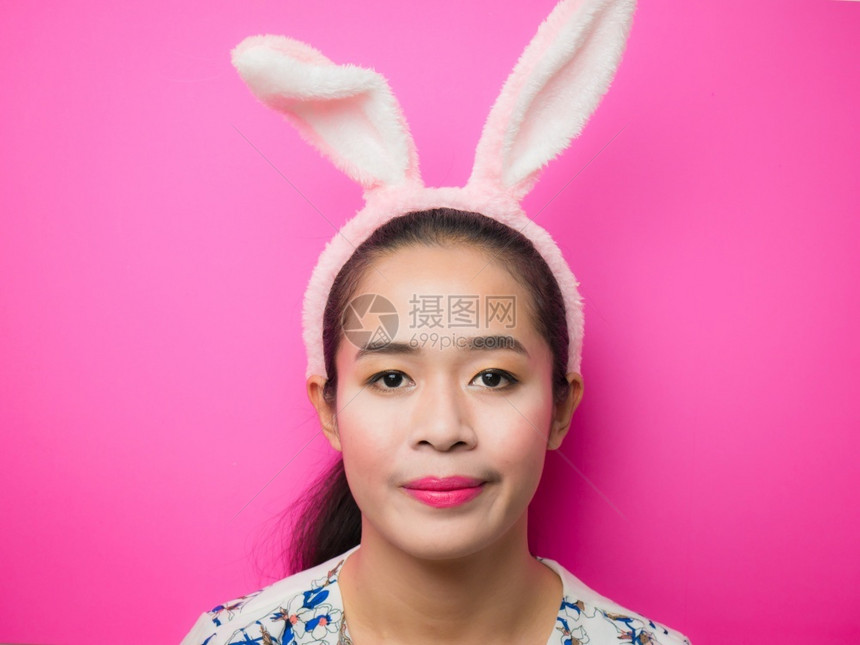 乐趣脸穿着兔子耳朵头带和粉红背景的可爱少女复活节时穿兔子耳朵头带的妇女在有吸引力的年轻女青中戴着兔子耳朵头带微笑着明亮的粉红背景图片