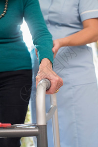八十年代老化高级女在与背景护理工作者一起行走的框架中手持重点背景图片