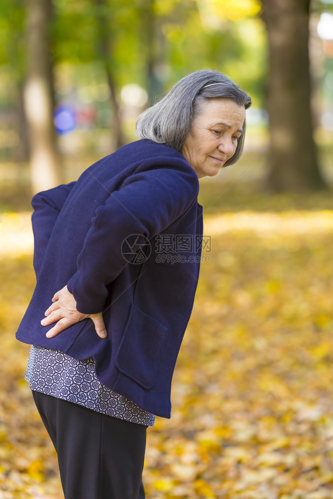 医生白种人秋天市公园的后背痛较轻老年妇女在秋天公园散步时感受到背痛疼的不快乐老年妇女户外图片