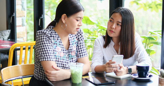 电话朋友们两个亚裔妇女在咖啡馆喝在智能手机上网购物友谊图片