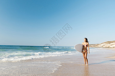 海滩上一个美丽的冲浪女孩拿着冲浪板图片