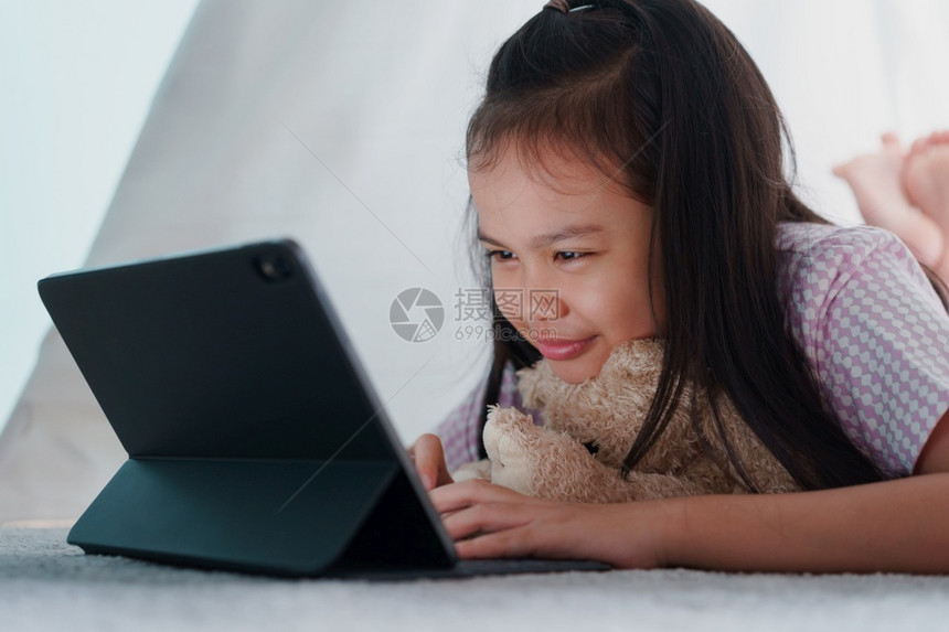 瞳孔游戏内部的亚洲小女孩在家晚上帐篷里使用平板电脑亚洲儿童在数字计算机上打工作图片