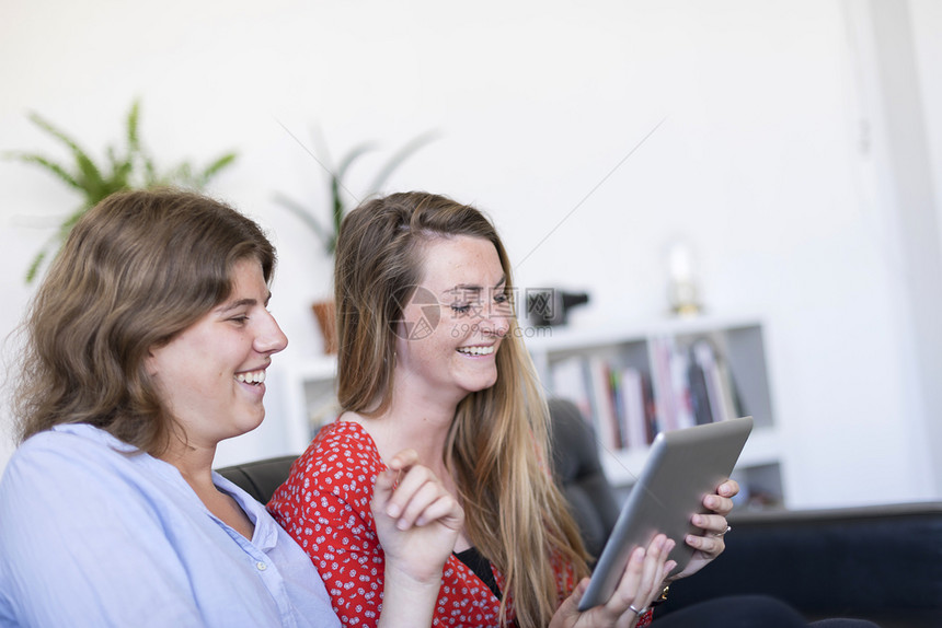 20多岁坐在沙发上或用平板电脑和微笑的石膏电脑在马地上坐着药片个人电脑图片
