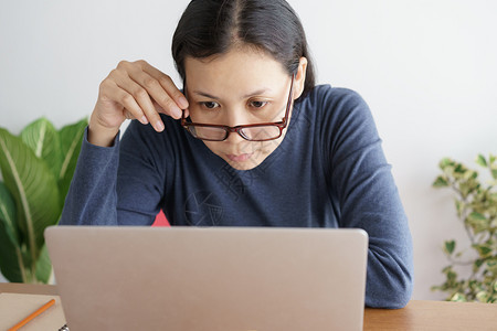 亚裔女在办公室工作她戴眼镜睛看笔记本电脑很认真办公室她桌子家图片