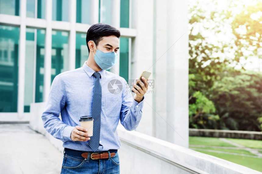 在新的正常生活方式概念中亚洲青年商人戴外皮面具和使用智能电话在城市保健中使用智能电话进行城市保健流感快乐的行病图片