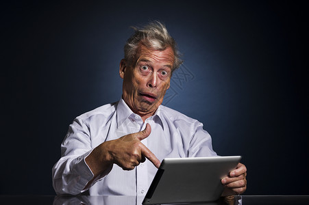 傻傻的惊喜商业傻的震惊老人用他手指着平板电脑看令人惊骇的难以置信和混乱幽默的上身工作室肖像画背景