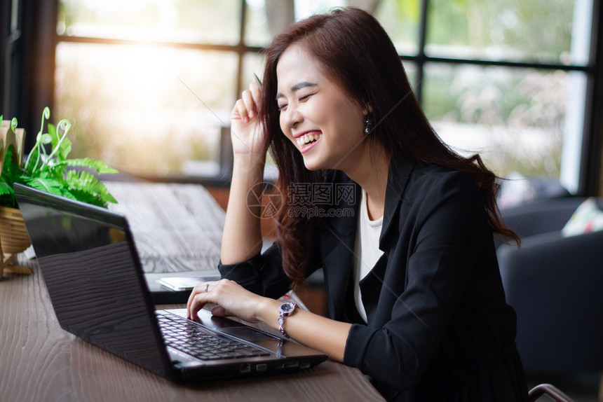 亚洲女商人在咖啡厅工作时微笑并使用笔记本电脑写现代的图片