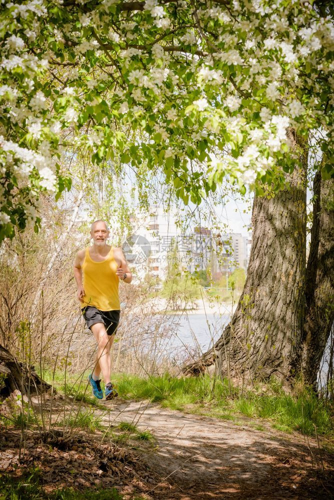公园oopicapi一名身穿黑黄衣的老人在温暖春日里在靠近湖边的森林里跑来去橙图片