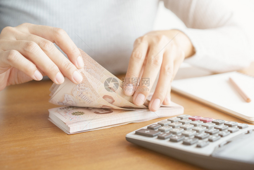 经济铢数近身手的亚洲女使用计算器和家庭内的钱图片