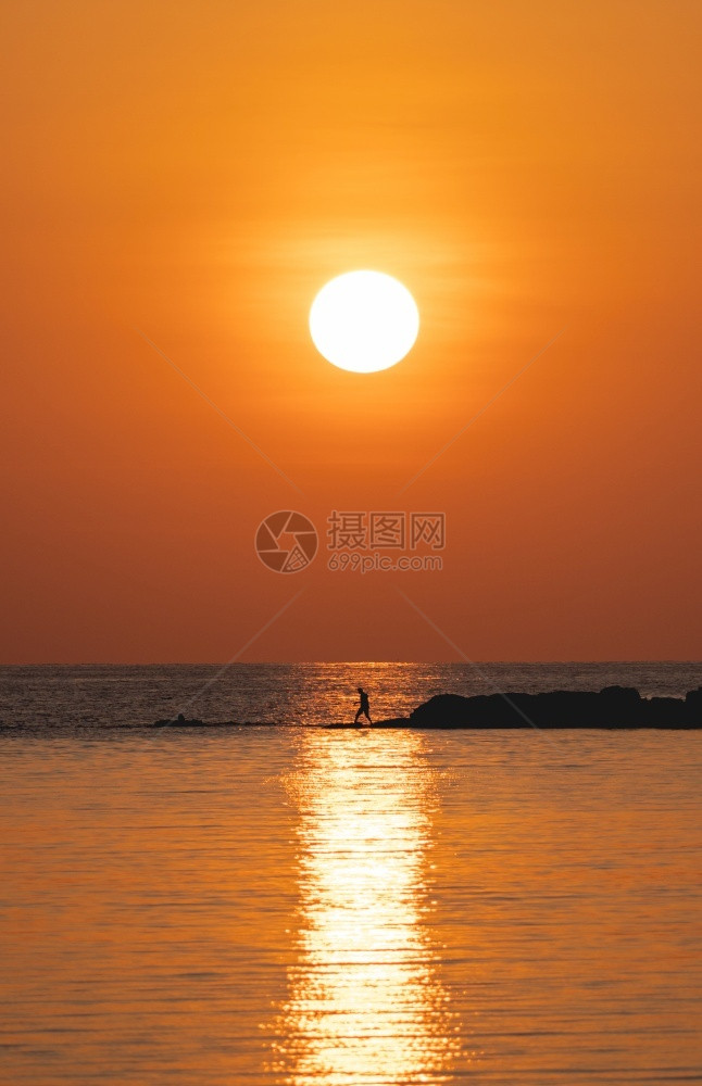 太阳在橙色天空海面上的太阳与岩石上有钓鱼棒的渔夫风景优美余辉日落图片