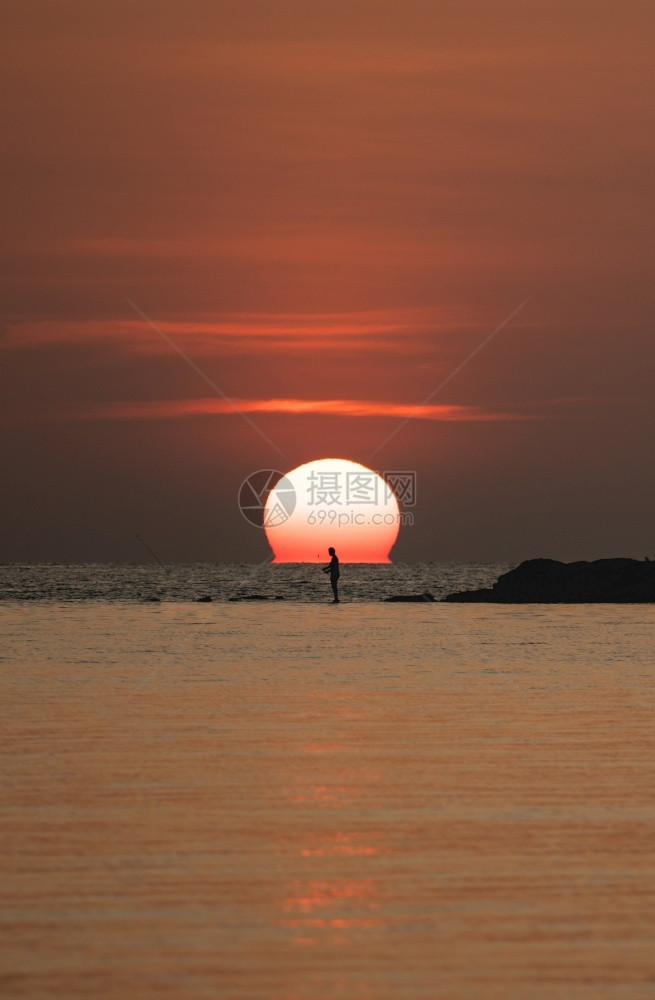 海浪水场景太阳在橙色天空海面上的太阳与岩石上有钓鱼棒的渔夫图片