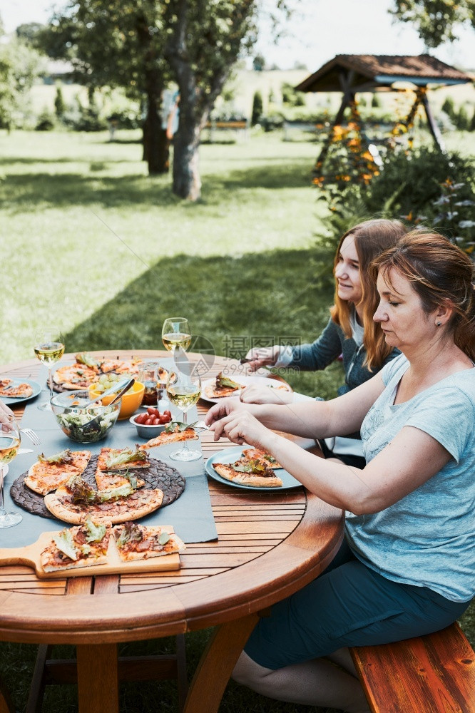 享受饮料家人和朋友在庭花园的夏季野餐户外晚期间用比萨沙拉水果和喝白葡萄酒在家庭花园的夏季野餐户外晚期间喝白葡萄酒桌子图片